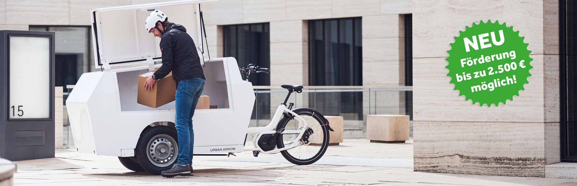 Paketbote legt Karton in die geöffnete Paketboxes eines weißen Urban Arrow Cargobikes