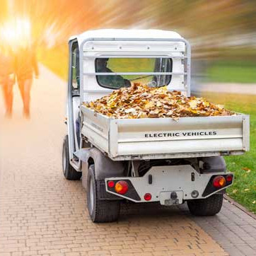 Elektromobil für Langschaftgärtner fährt auf einem Fußgängerweg. Die Ladefläche ist gefüllt mit Laub